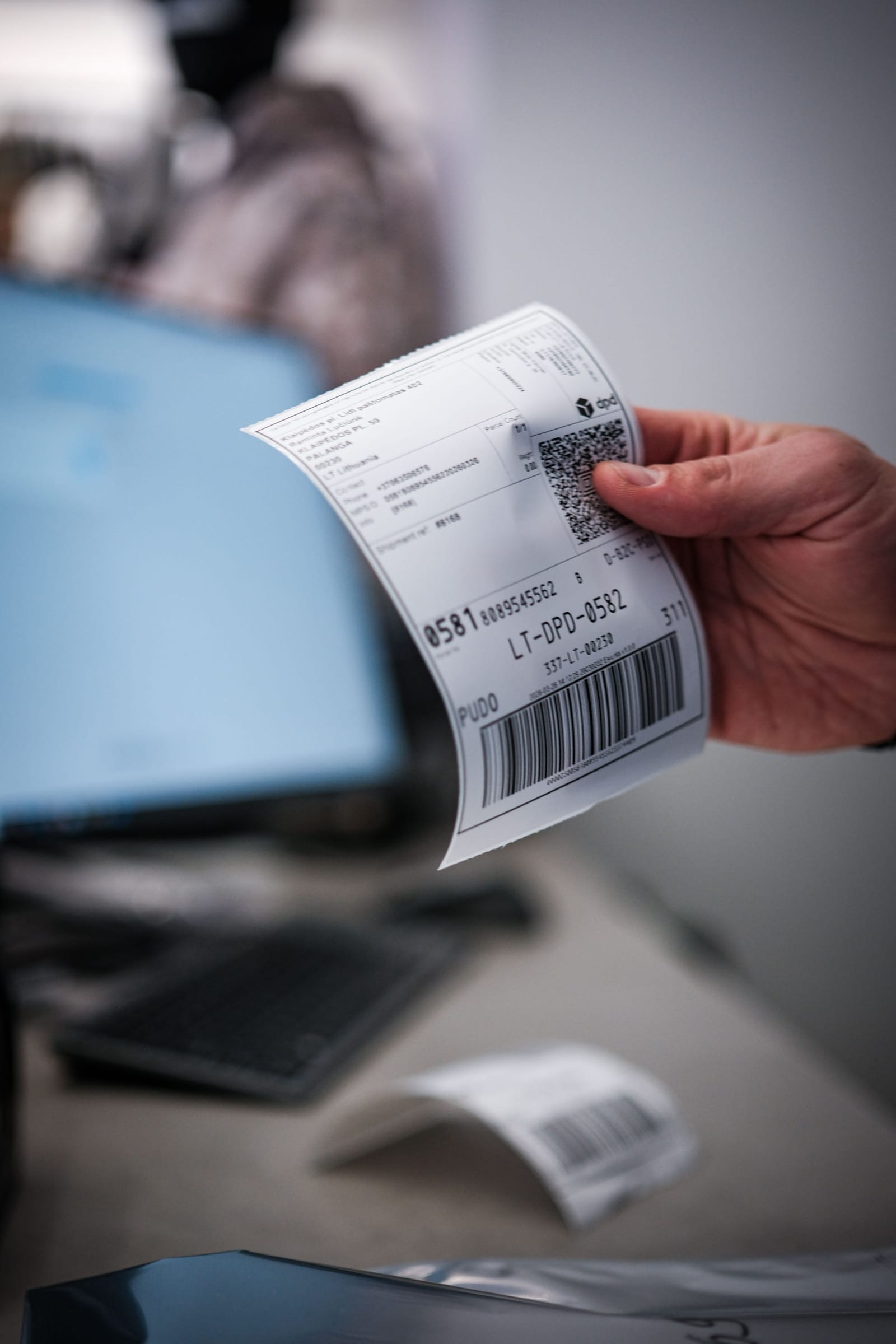 A hand holding a printed DPD shipping label with a barcode